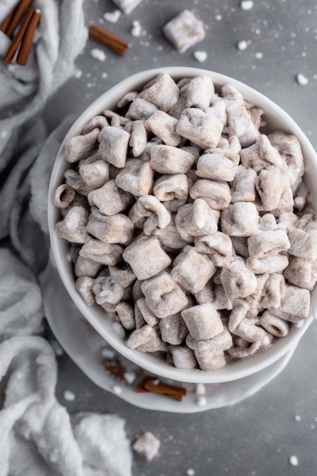 A high-resolution photo of cinnamon roll Puppy Chow dusted heavily with powdered sugar, in a white bowl under soft lighting.